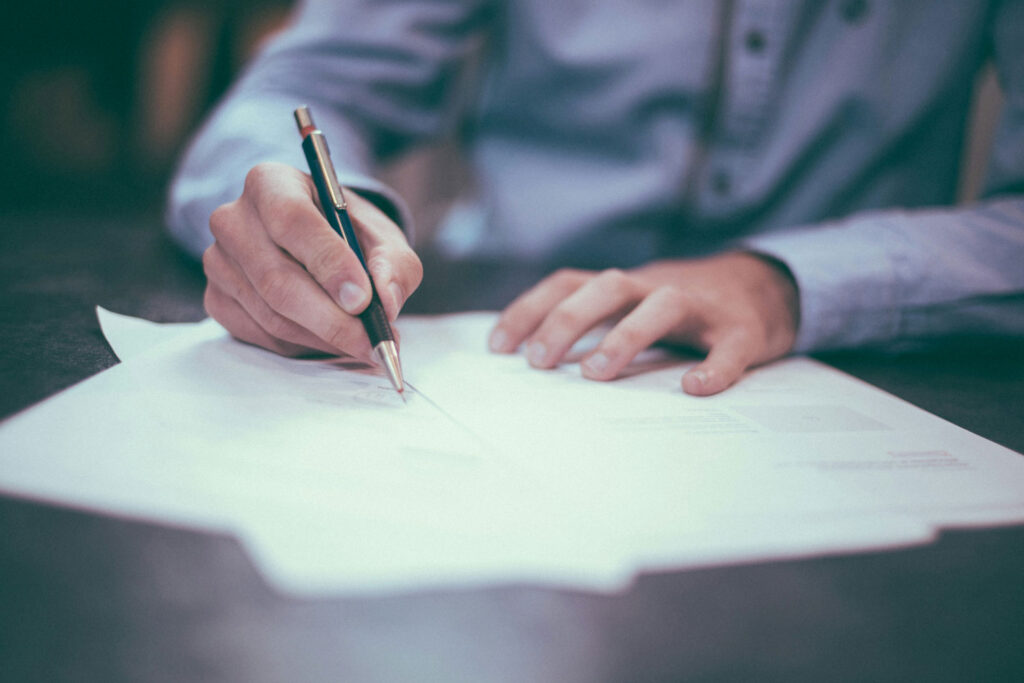 An individual jotting down notes on a sheet of paper with a pen.