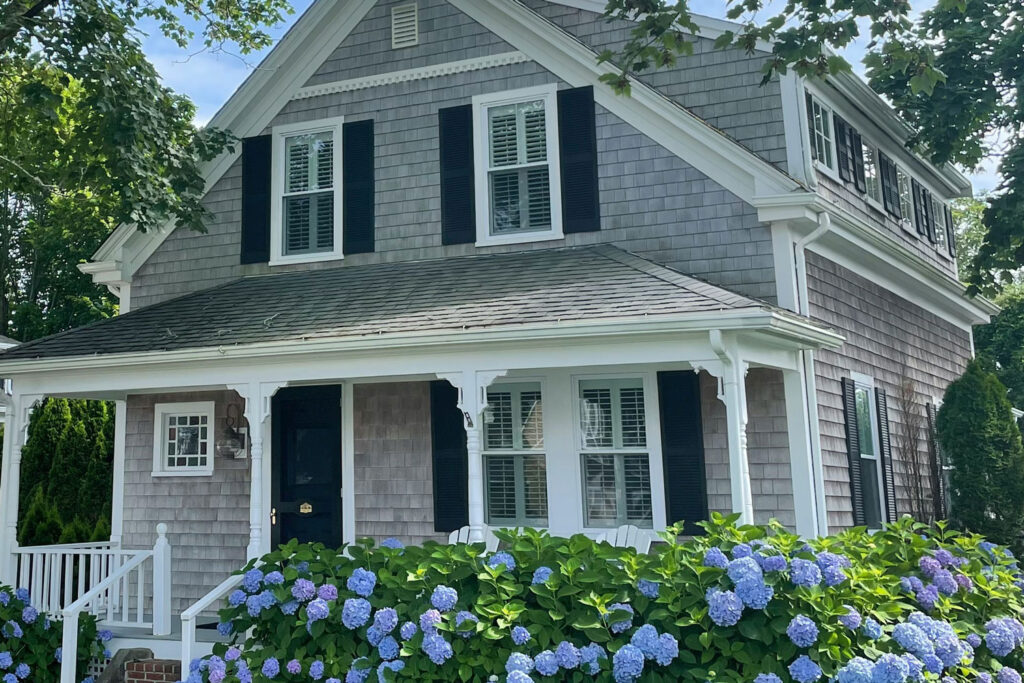 Gray cedar shingled house with blue hydrangea flowers in front.